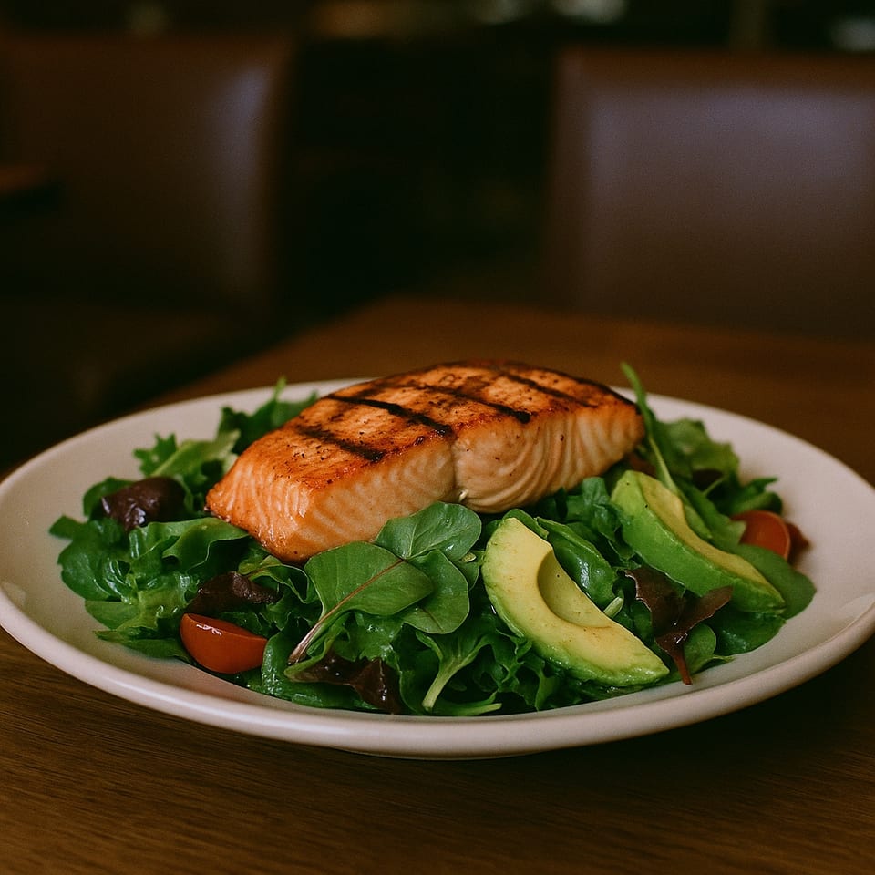 Grilled salmon fillet with grill marks, served on a bed of fresh greens, avocado, and cherry tomatoes.